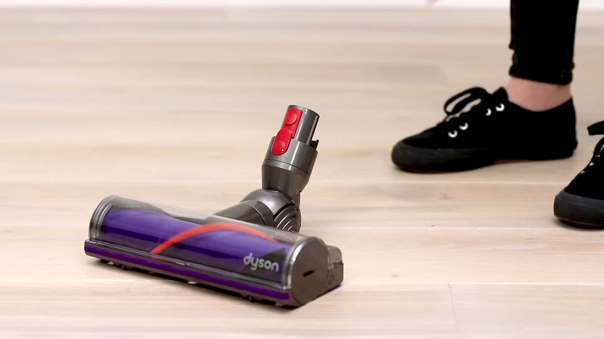 Dyson V10 Absolute vacuum nozzle on hardwood floor with user's feet nearby