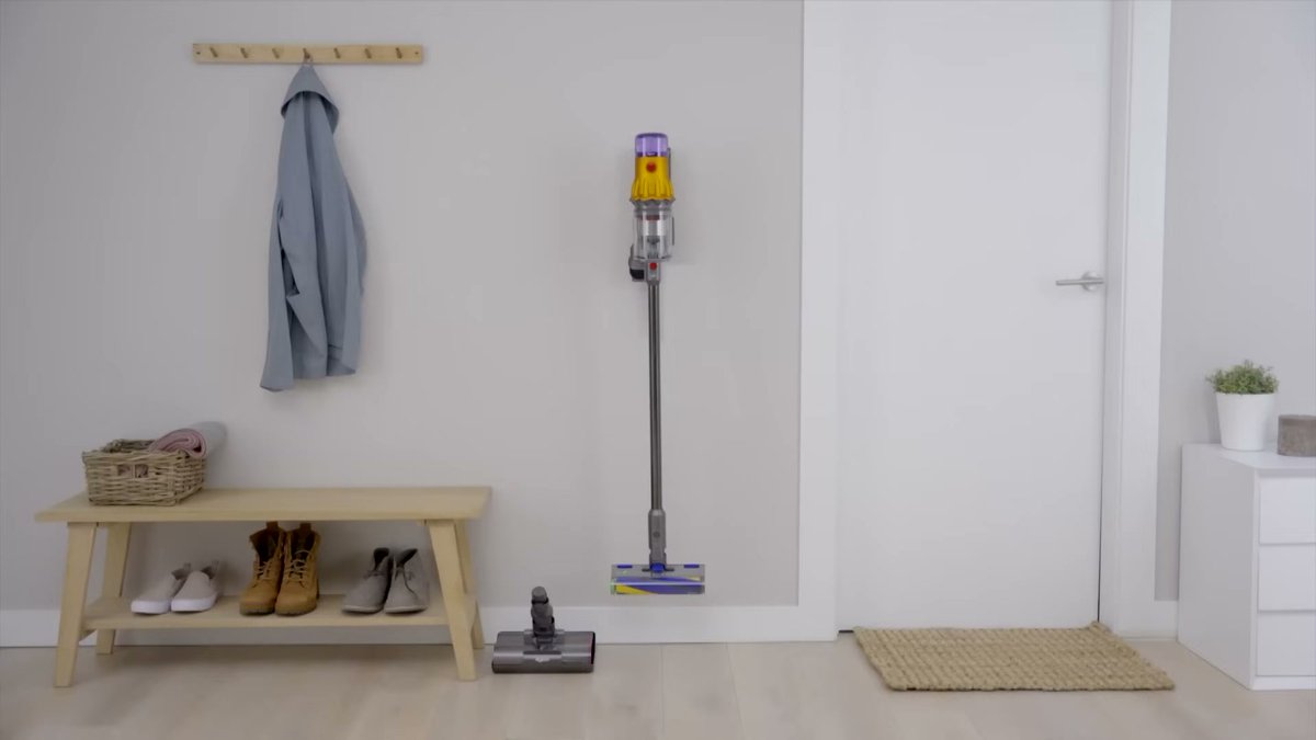 Dyson V12 Detect Slim standing upright on hardwood floor in entryway with shoes and coat rack nearby